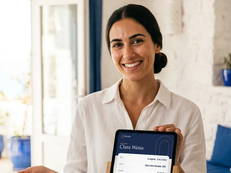 A boutique hotel receptionist in Athens turns a check-in tablet toward a guest.